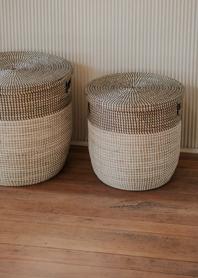 Large and small lidded baskets displayed side by side against a softly striped wall.