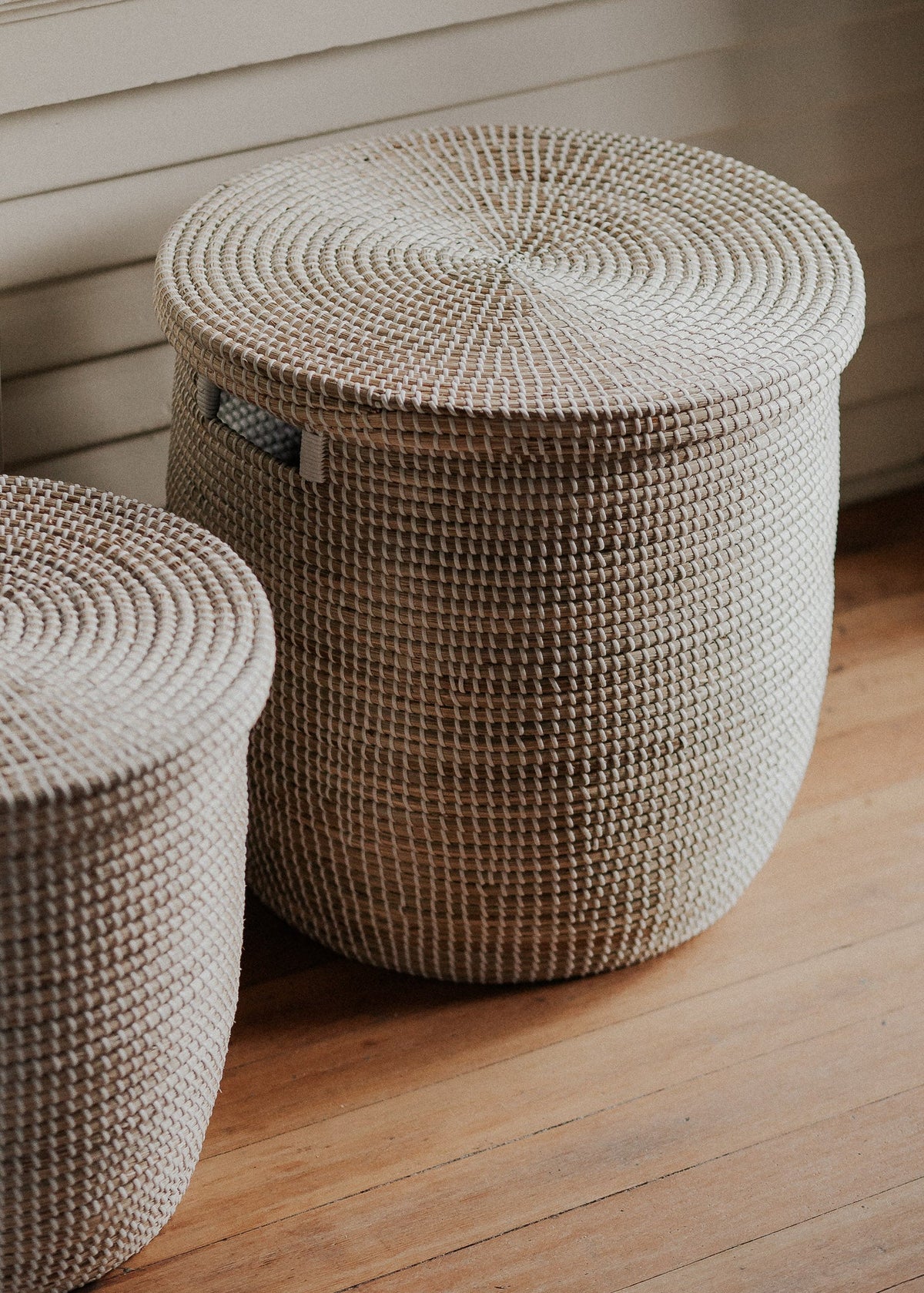 Close lifestyle view of the large lidded basket on a wood floor, highlighting its natural fibers and spiral lid pattern.