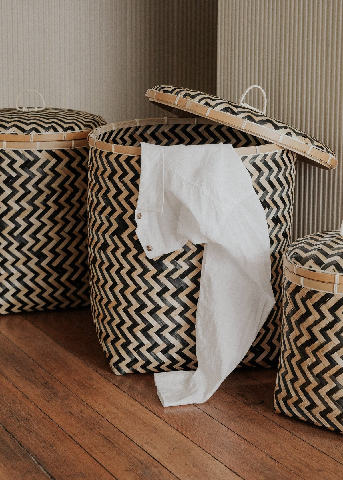 Java baskets used as laundry hampers, with white fabric draped from the open medium basket.