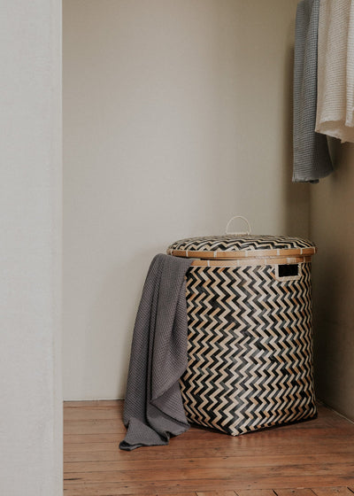 Large lidded Java basket styled in a bedroom corner beside a gray textile.
