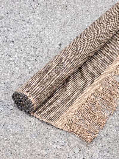 Korissa Goldilocks Rug, natural colorway, rolled up on concrete floor