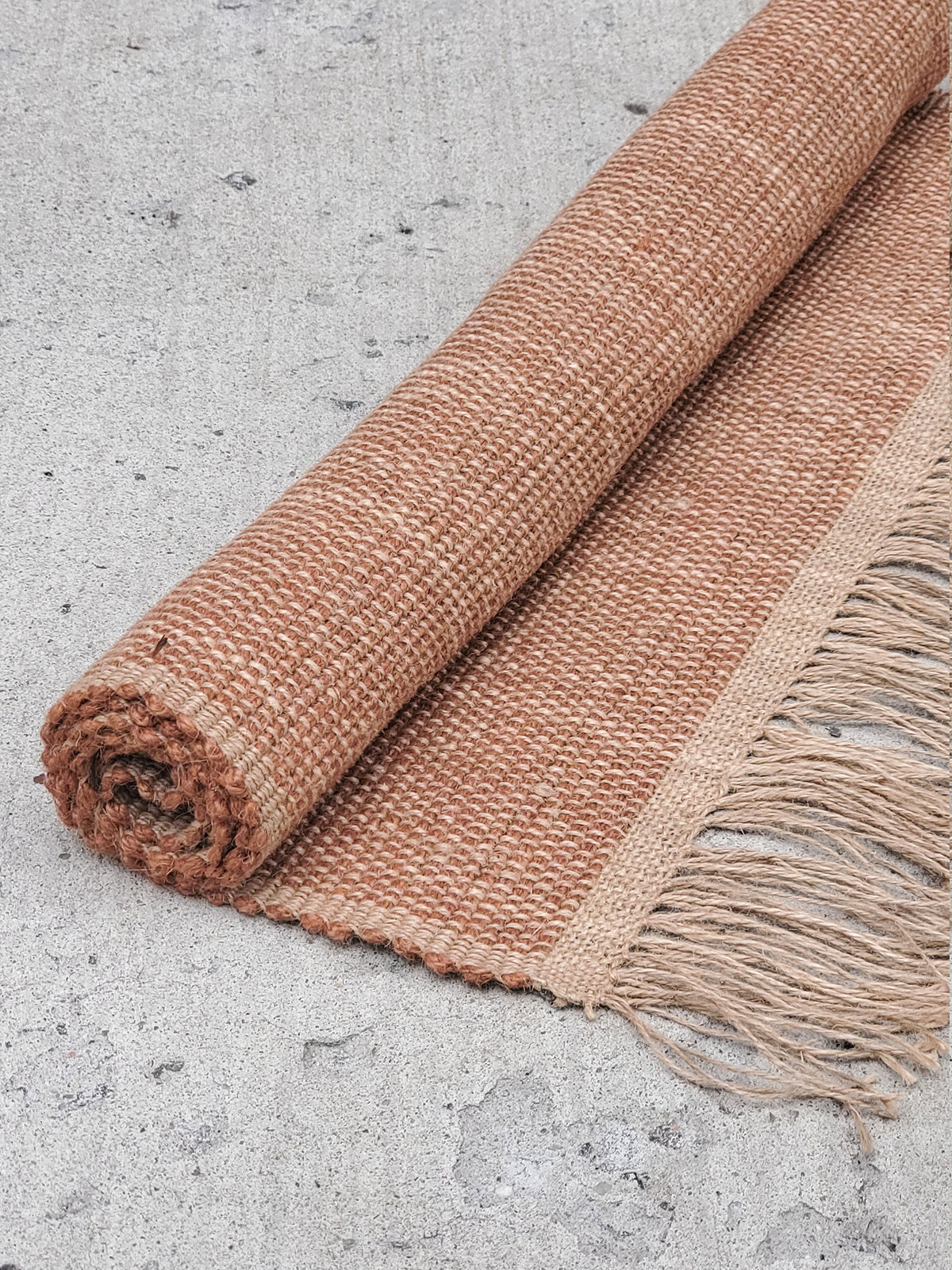 Korissa Goldilocks Rug, brown colorway, rolled up on concrete floor