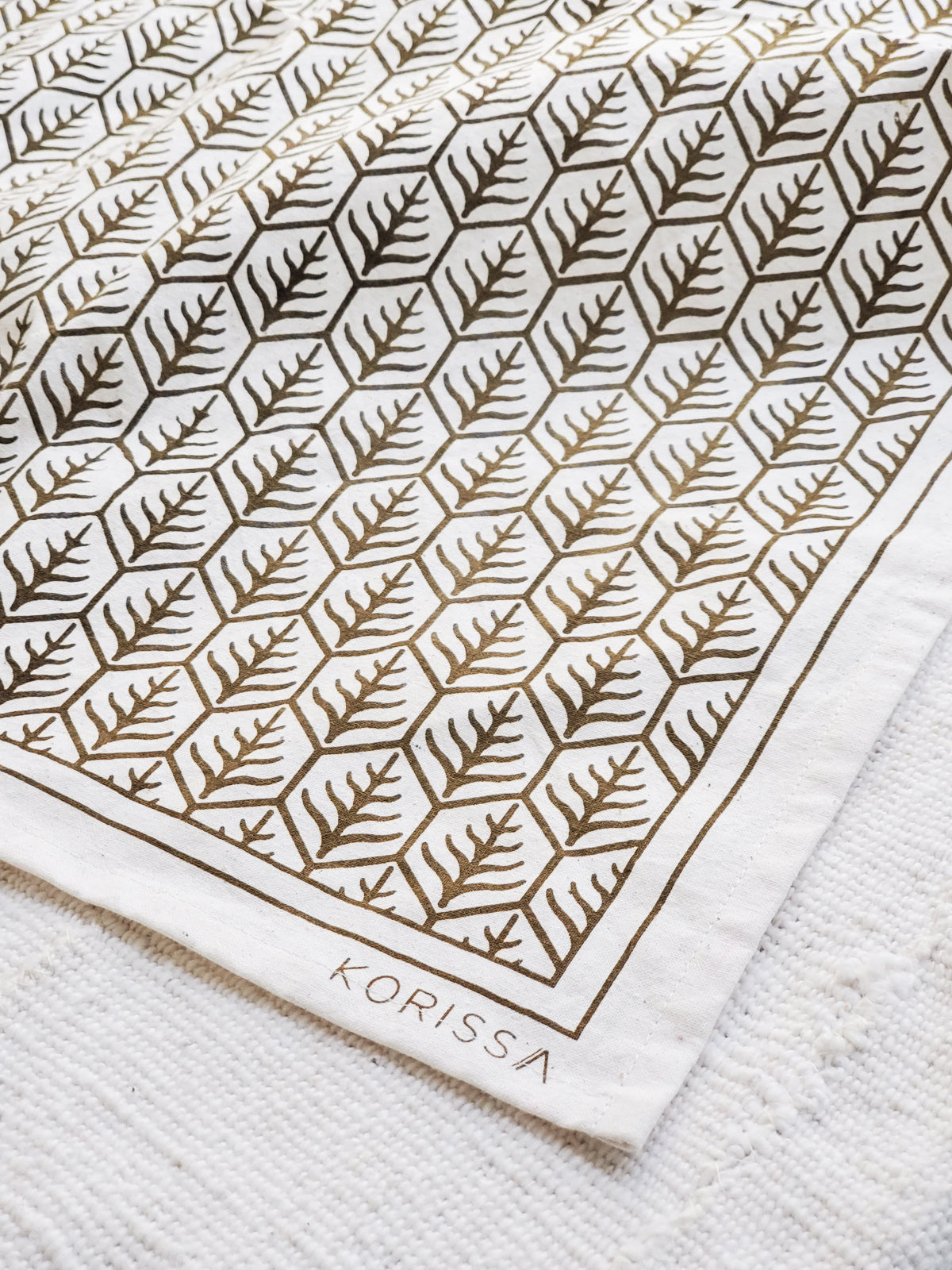Korissa Hand Screen Printed Tea Towel, dark brown print, on woven natural-fiber mat