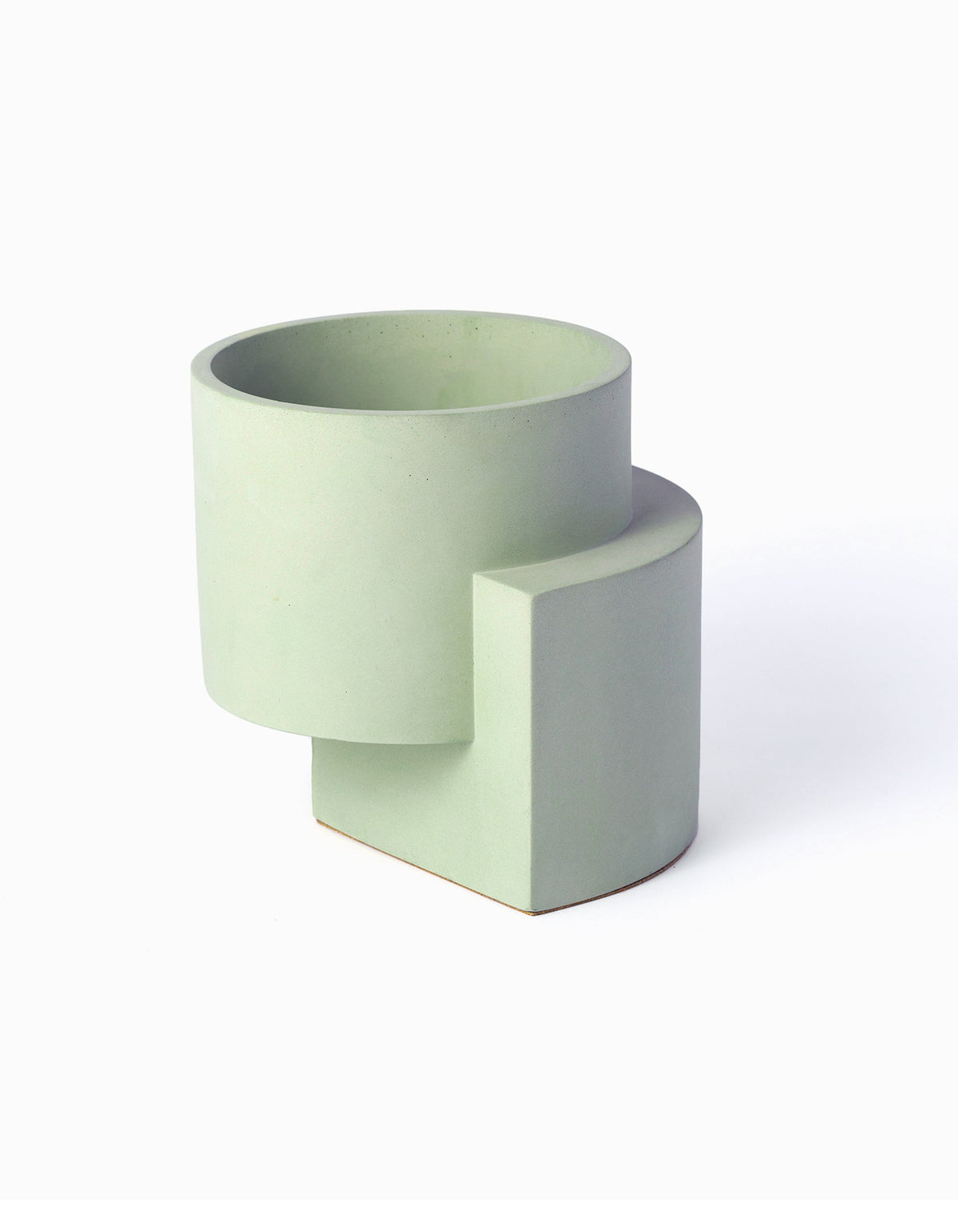Pale green Tortuga Forma Platform Planter Medium - Polished Concrete viewed at an angle on white, showing an open cylindrical bowl raised above a curved vertical support, with a smooth surface and scattered tiny pores.