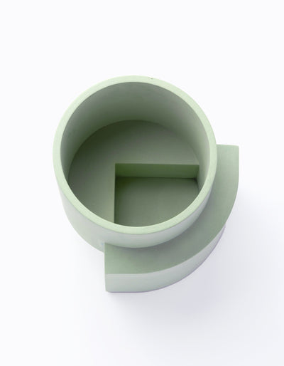 Overhead view into a pale green Tortuga Forma Platform Planter Medium - Polished Concrete, showing its thick circular rim, empty interior and a rectangular raised section inside the bottom.