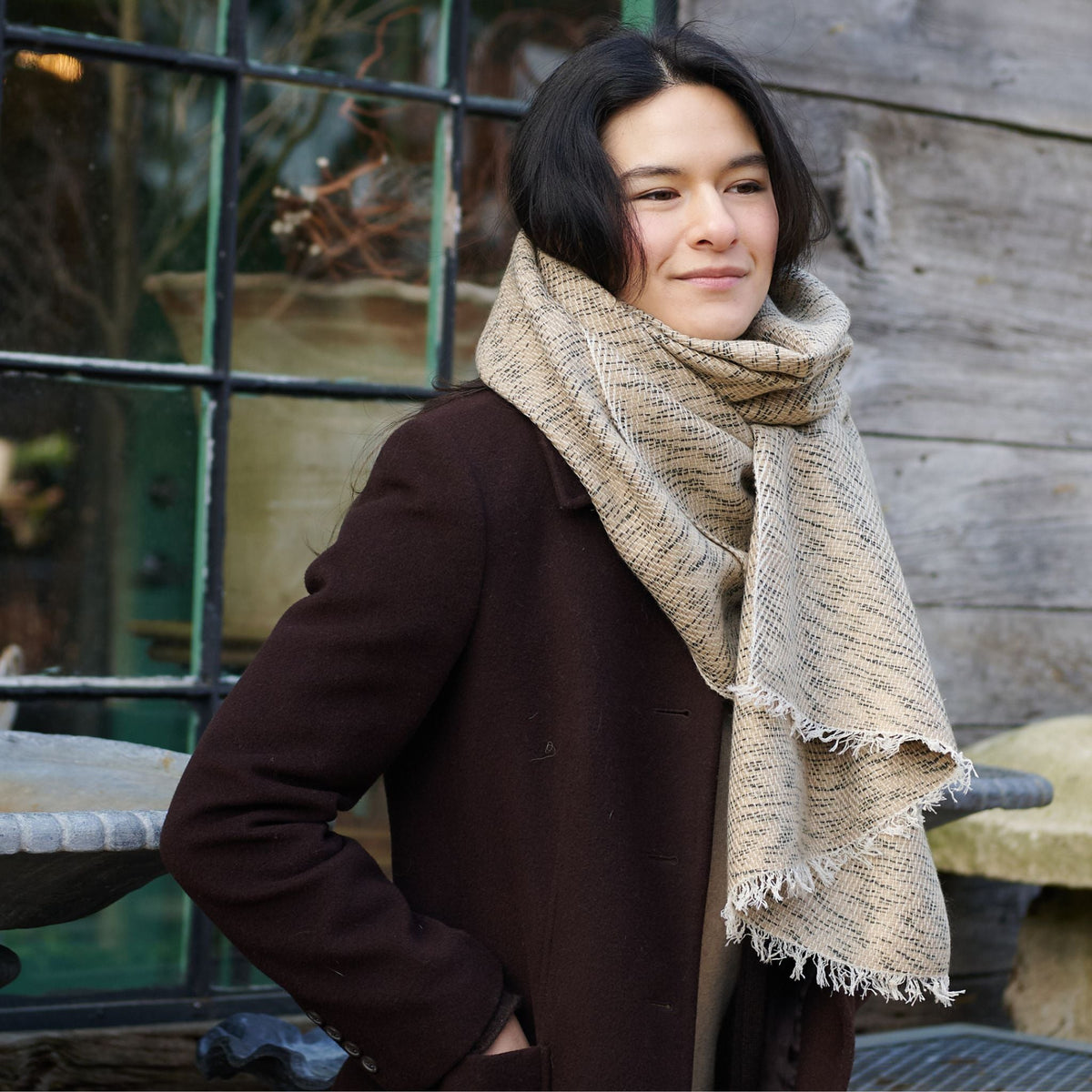 Woman outdoors wearing the fringed neutral scarf with a dark brown coat.