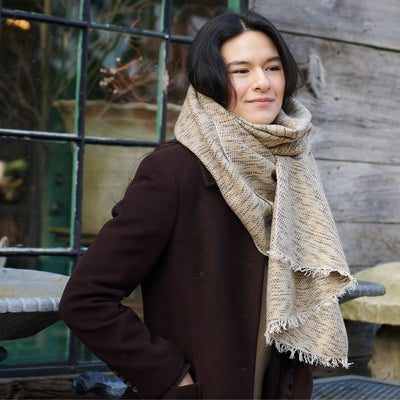 Woman outdoors wearing the fringed neutral scarf with a dark brown coat.