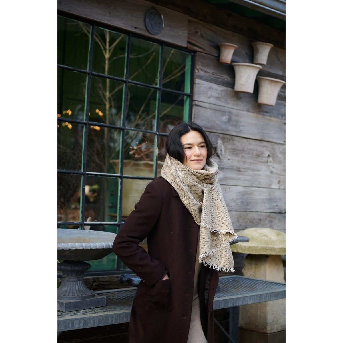 Full-length outdoor view of a woman wearing the neutral scarf with a long brown coat.