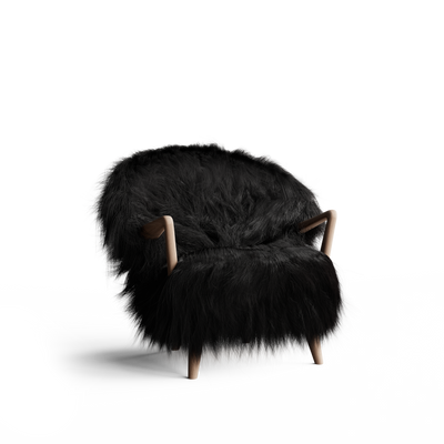 Three-quarter front view of the Eikund Fluffy Lounge Chair against white, showing long black shaggy upholstery, a broad rounded back, a deep seat, sculpted light wood armrests, and short tapered wood legs.
