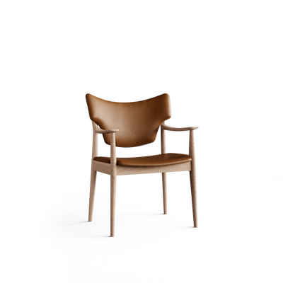 Three-quarter front view of the Eikund Veng Arm Chair with cognac-brown upholstery and a light wood frame, showing a wing-shaped curved back, slim padded seat, sculpted armrests, and tapered legs.