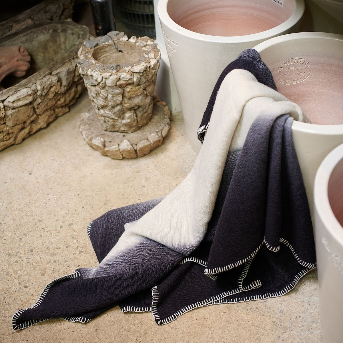 Ink Black and White throw draped beside handmade ceramic vessels, with its black, cream and stitched edges visible