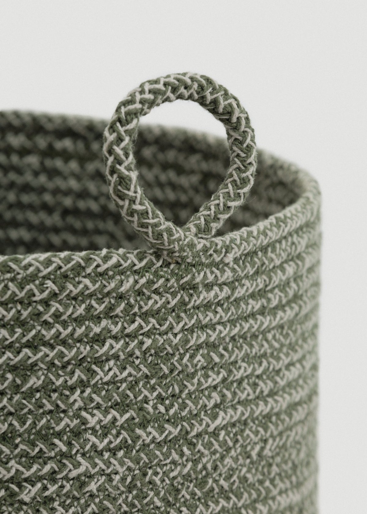 Close-up of the green-and-cream braided rope, rounded rim, and circular loop handle.