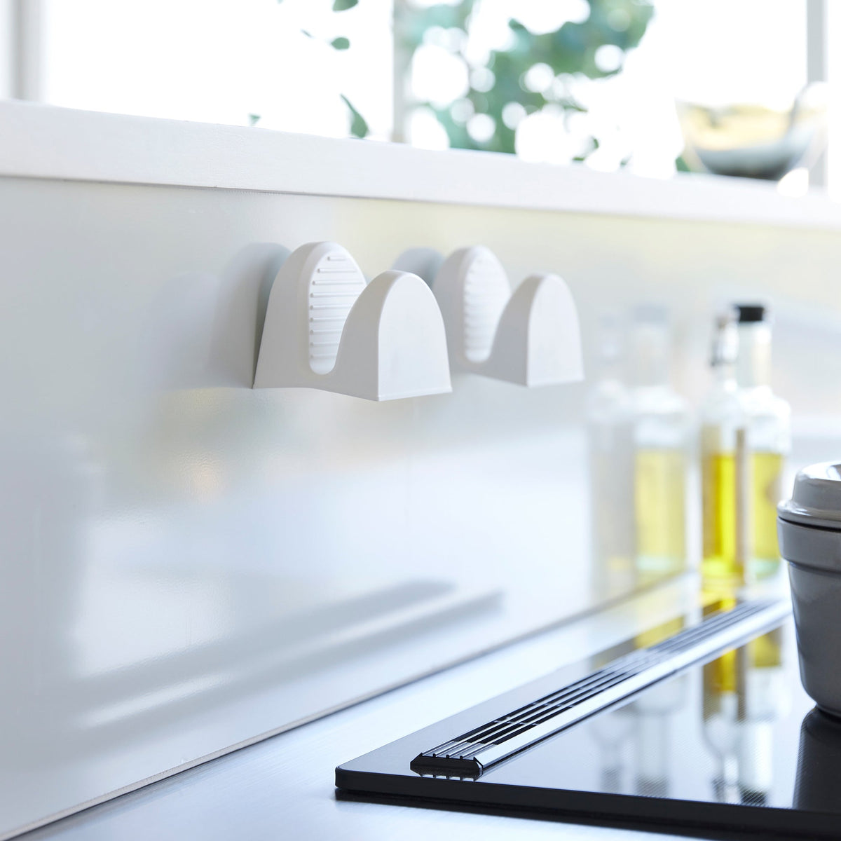 Two white Yamazaki Home Magnetic Pot Holders - Set of 2 - Silicone stored side by side on a kitchen backsplash, showing their arched profiles and ribbed inner surfaces.