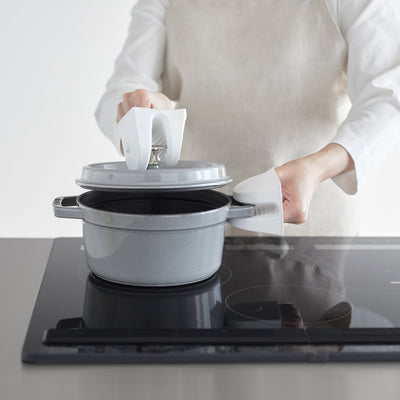 Person uses white Yamazaki Home Magnetic Pot Holders - Set of 2 - Silicone to lift a grey pot lid while steadying the pot by its side handle.