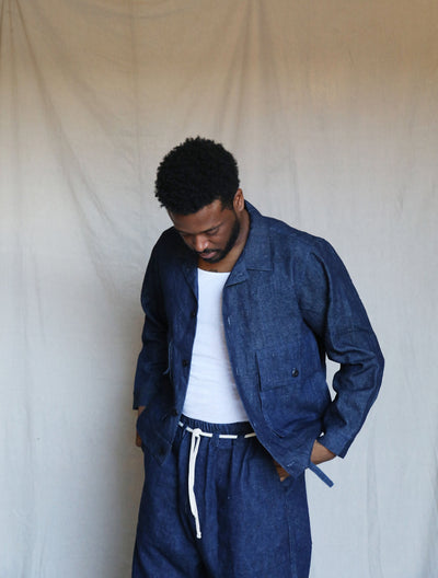 Model looking down while wearing the indigo Studio Coat over a white shirt and matching pants.