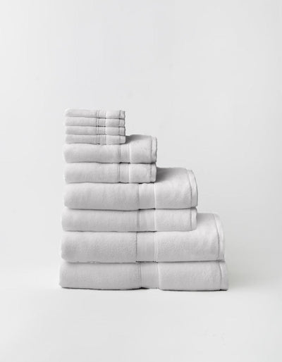Light gray towels stacked in a stepped arrangement on a pale background, showing multiple sizes, thick folded edges, and woven border bands.