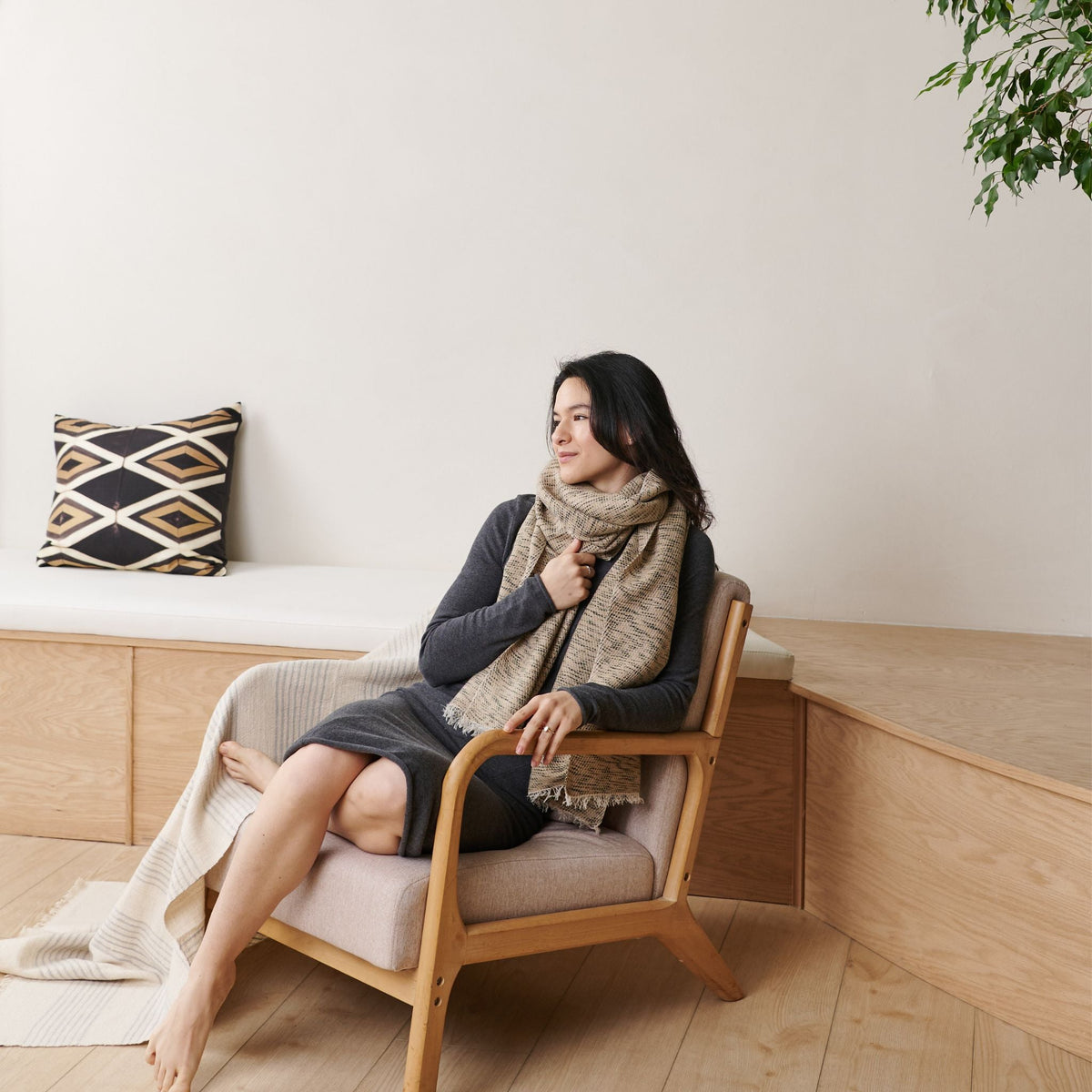 Woman seated in a wooden lounge chair with the neutral scarf wrapped warmly around her neck.