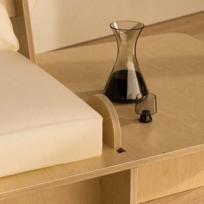 Integrated natural wood side platform on the Franklin Low Seater holding a glass carafe and small drinking glass