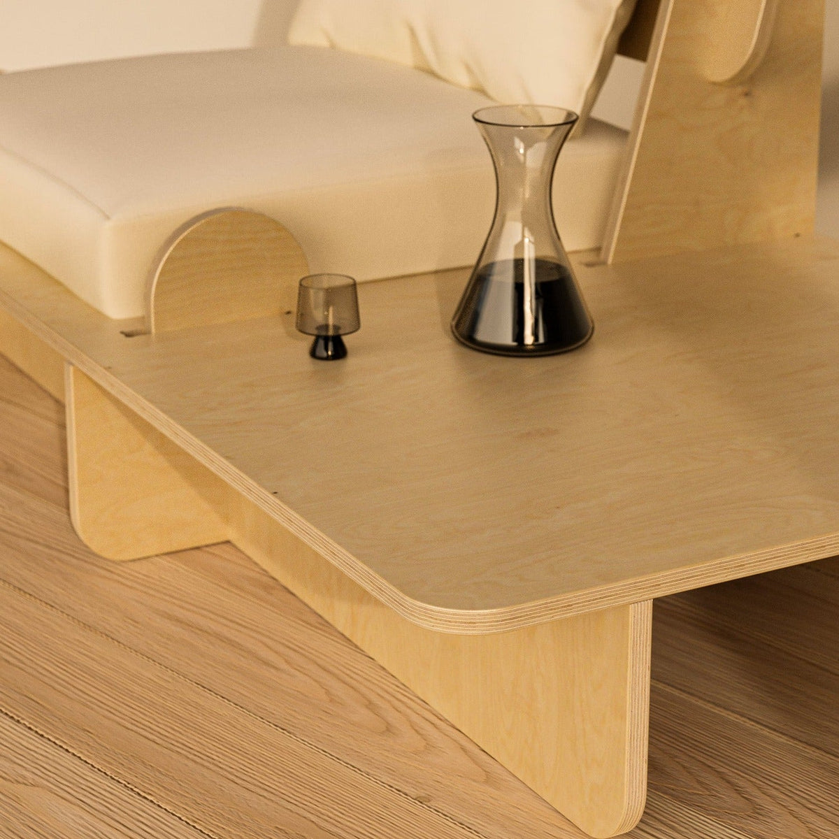 Close-up of the Franklin Low Seater’s rounded wood side platform holding a glass carafe and drinking glass