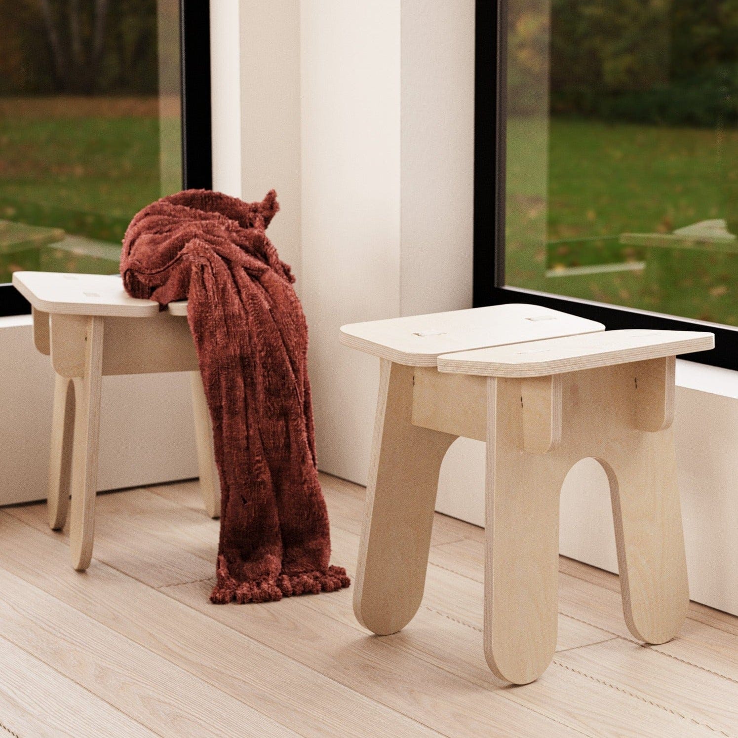 Two BURIJ natural wood stools beside large windows, with a rust-colored knitted throw draped over one stool
