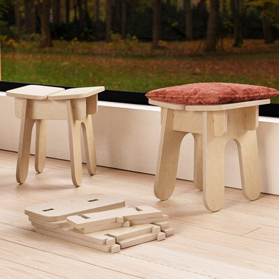 Two BURIJ wood stools beside a large window, one topped with a rust cushion and unassembled stool components arranged on the floor