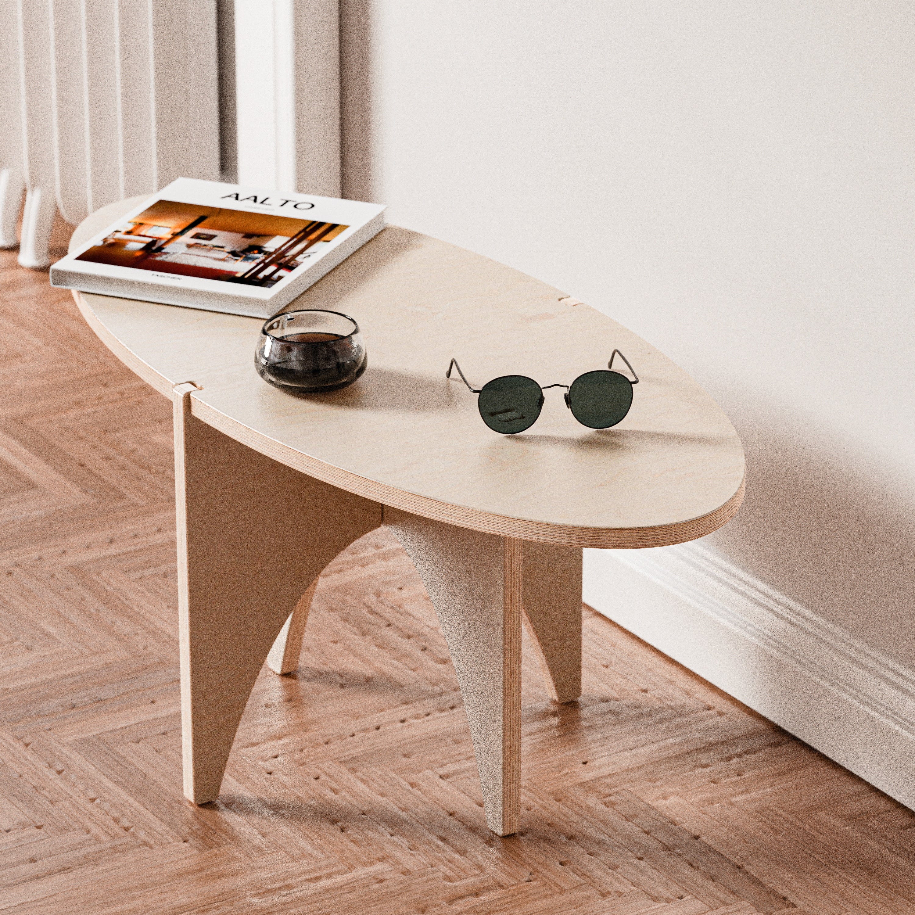 Close angled view of the YOYO accent table showing its pale oval wood top, curved panel base, magazines, candle and sunglasses