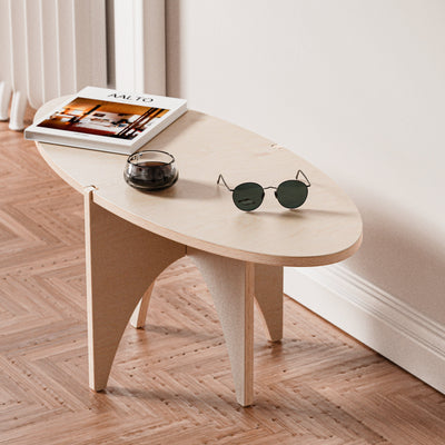 Close angled view of the YOYO accent table showing its pale oval wood top, curved panel base, magazines, candle and sunglasses