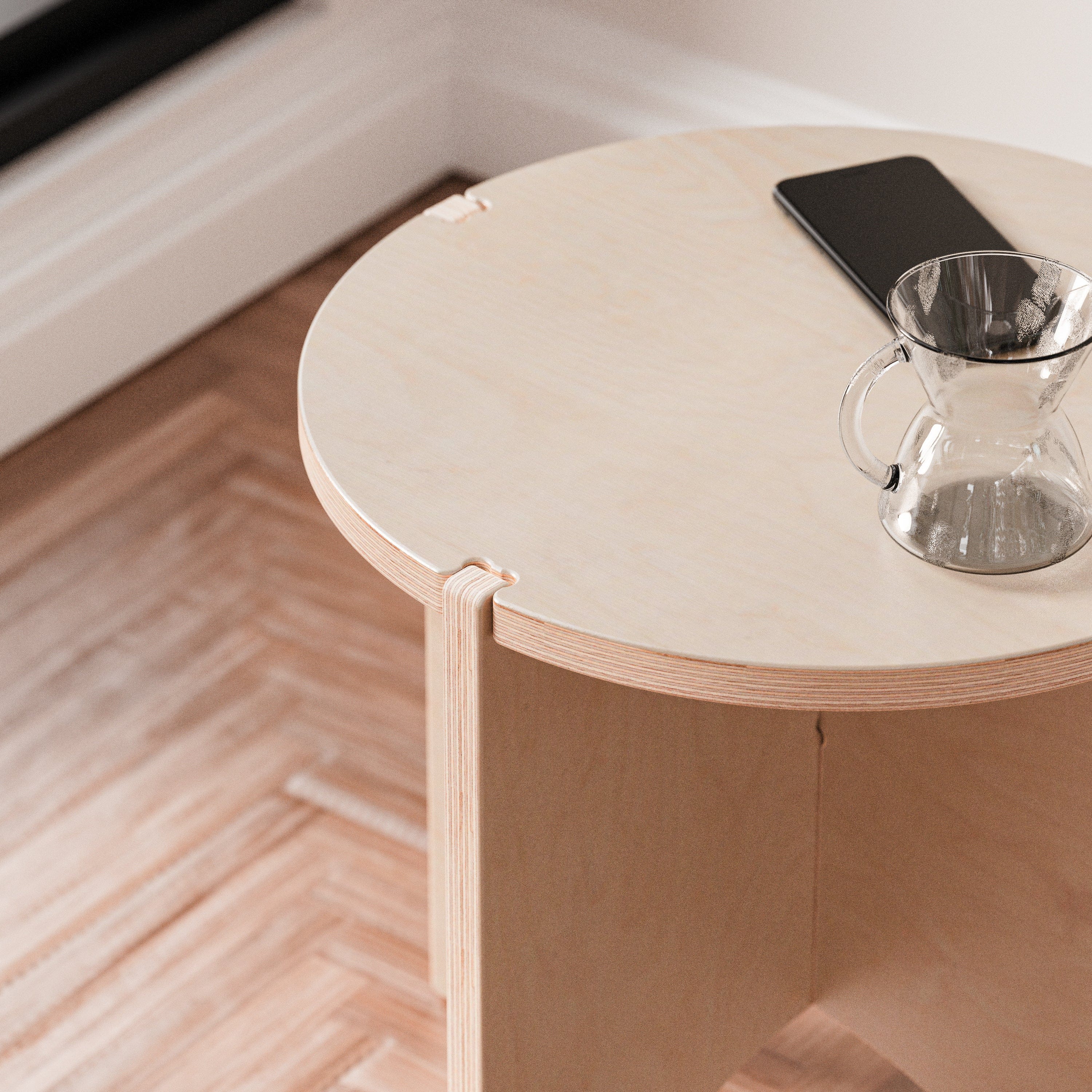 Close-up of the YOYO end table’s round pale wood top holding a smartphone and a glass of water