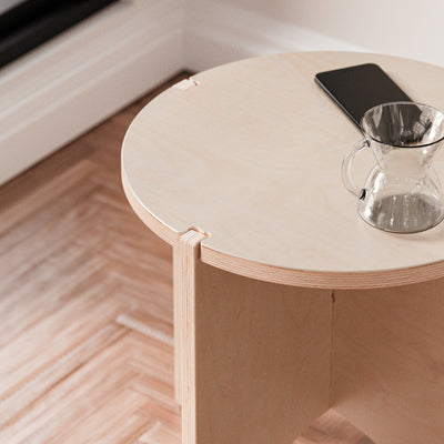 Close-up of the YOYO end table’s round pale wood top holding a smartphone and a glass of water