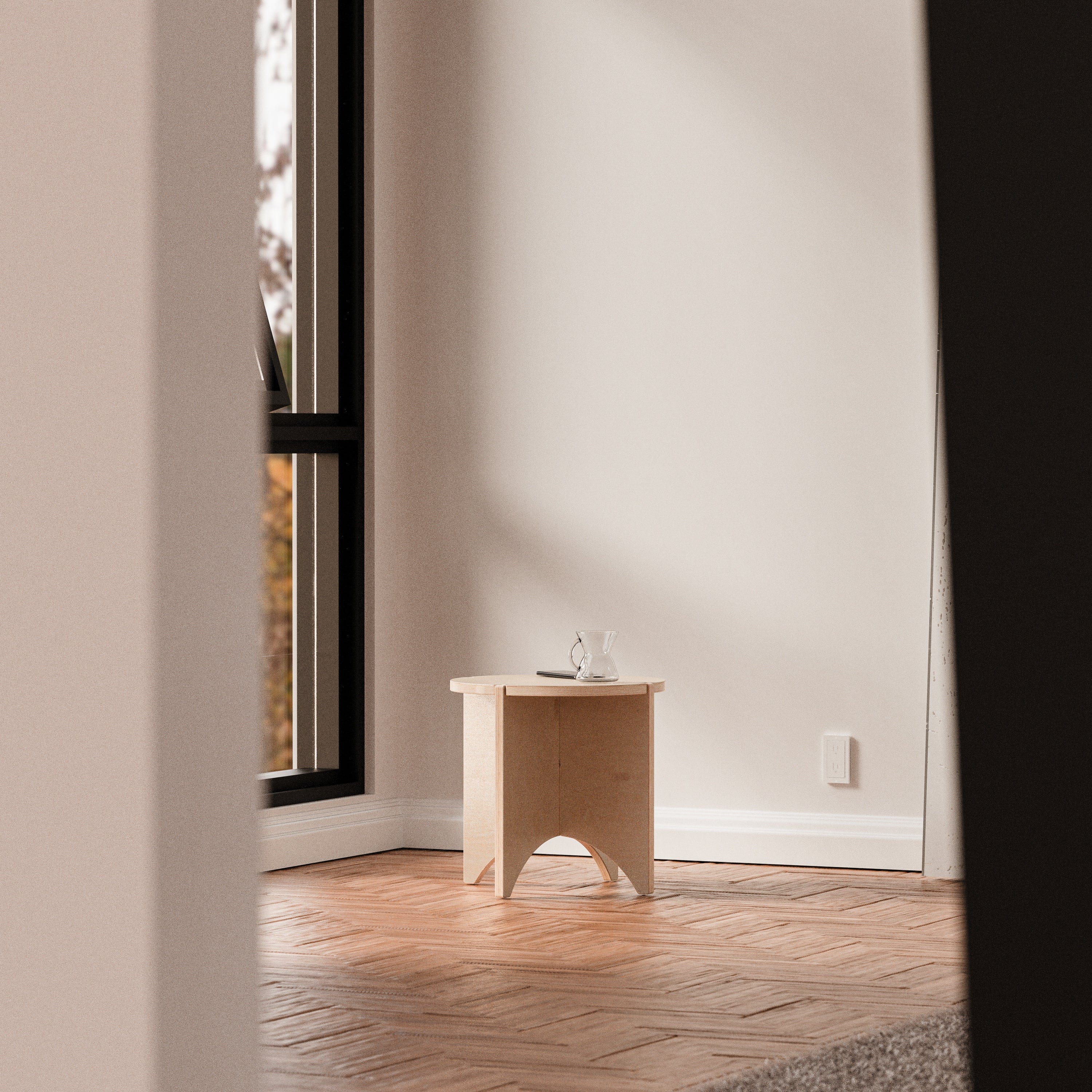 YOYO natural wood end table standing alone against a white wall in a spacious minimalist room with herringbone floors