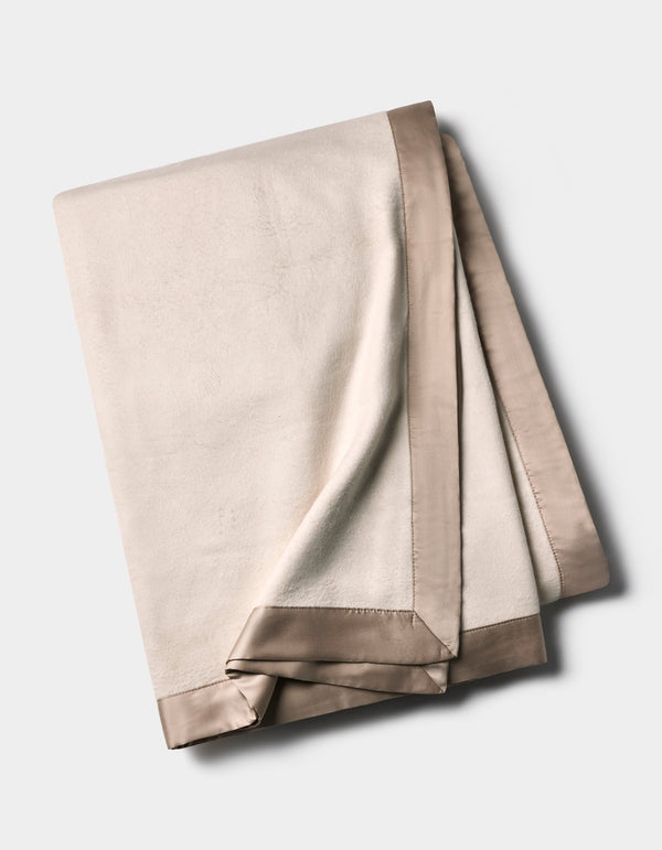 Ivory Bamboo Blanket folded on a pale background, showing a softly textured surface and wide taupe satin border with neatly finished corners.