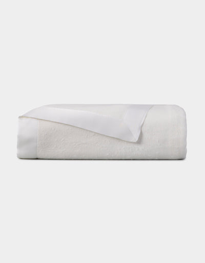 White blanket folded into a compact rectangular stack, with one corner turned back to reveal the matching satin border.