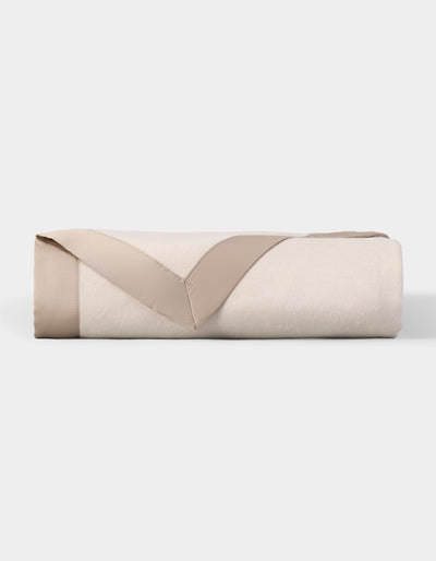 Ivory blanket folded into a rectangular stack, with its taupe satin border turned back in a V shape across the front.