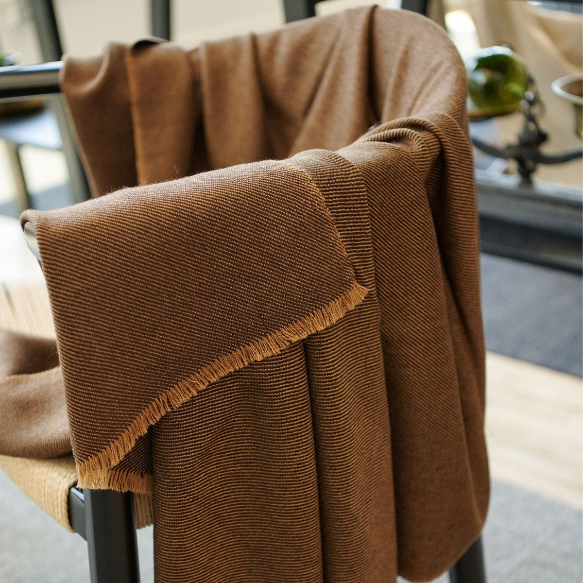 Hay Brown merino throw layered over the back and arm of a chair, showing its soft drape, fine twill weave and fringed edge