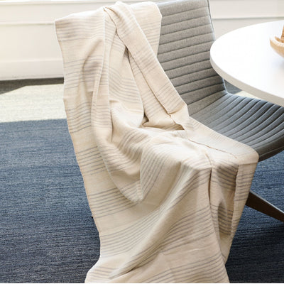 Silica Chalk striped throw loosely draped over a gray upholstered dining chair beside a white table