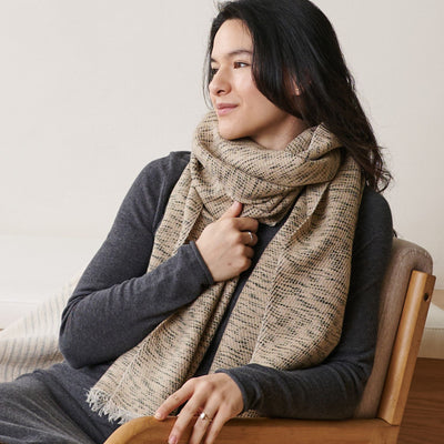 Close view of a seated woman wearing the thick beige scarf over a charcoal-gray top.