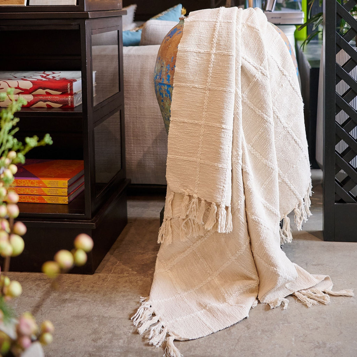 Sea Shell White textured throw hanging vertically in a colorful textile shop, displaying its subtle check pattern and fringe