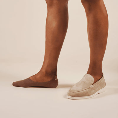 Person wearing brown socks and beige loafers on a plain background