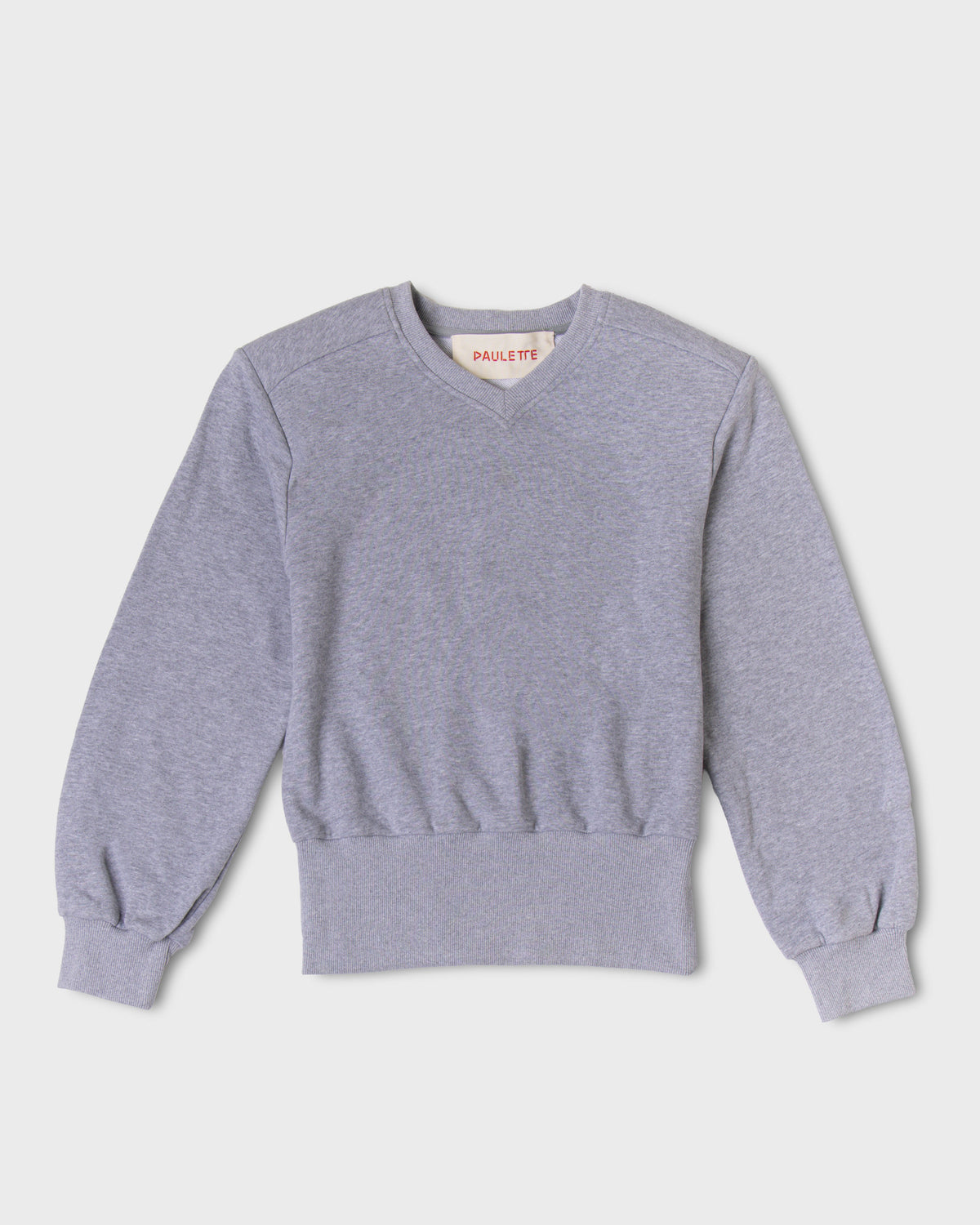 Light gray Paulette Madeleine Top displayed against a light background, showing a shallow V-neck, structured shoulders, loose sleeves gathered into ribbed cuffs, and a broad ribbed hem.