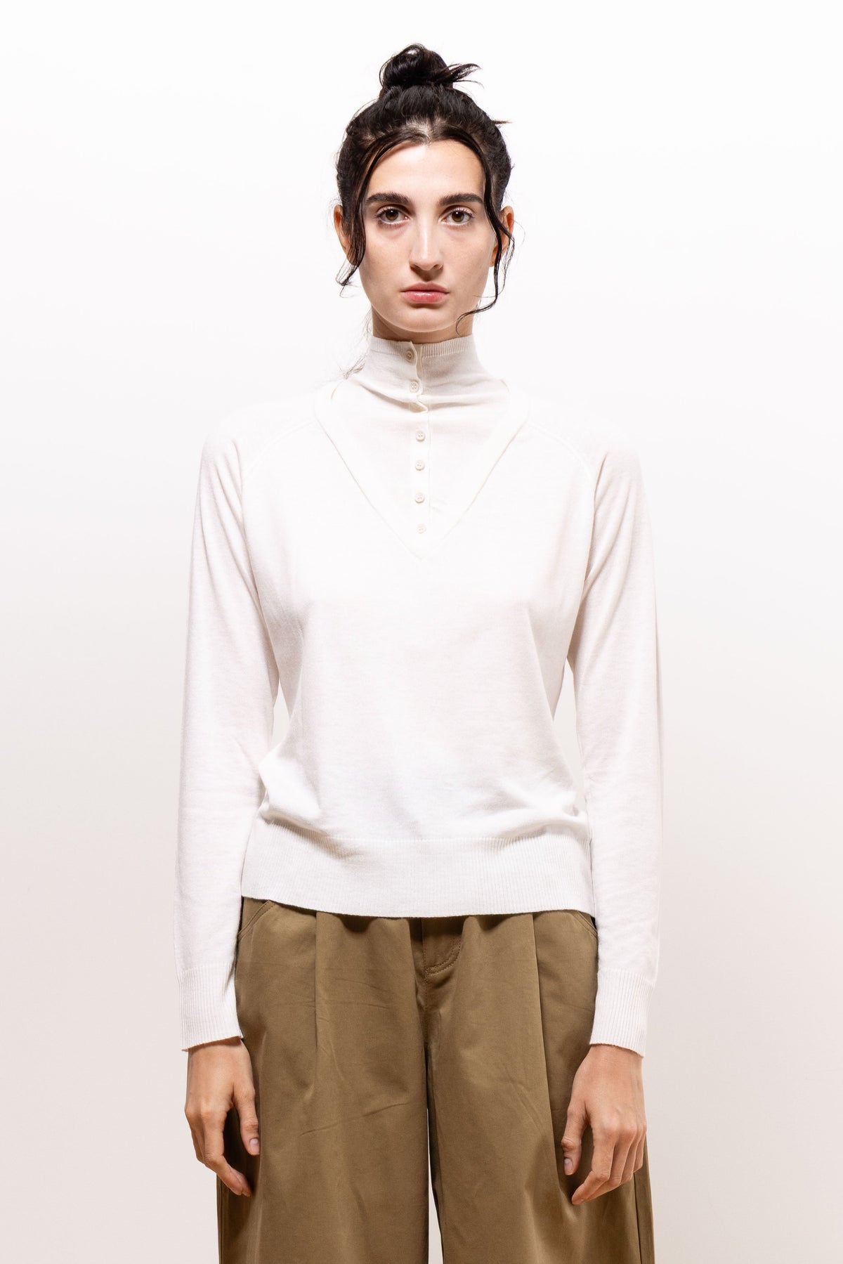 Front view of a model wearing the ivory Paulette Montagne Top with khaki-brown trousers, arms relaxed at her sides, showing the high collar, shoulder gathers, and hip-length hem.