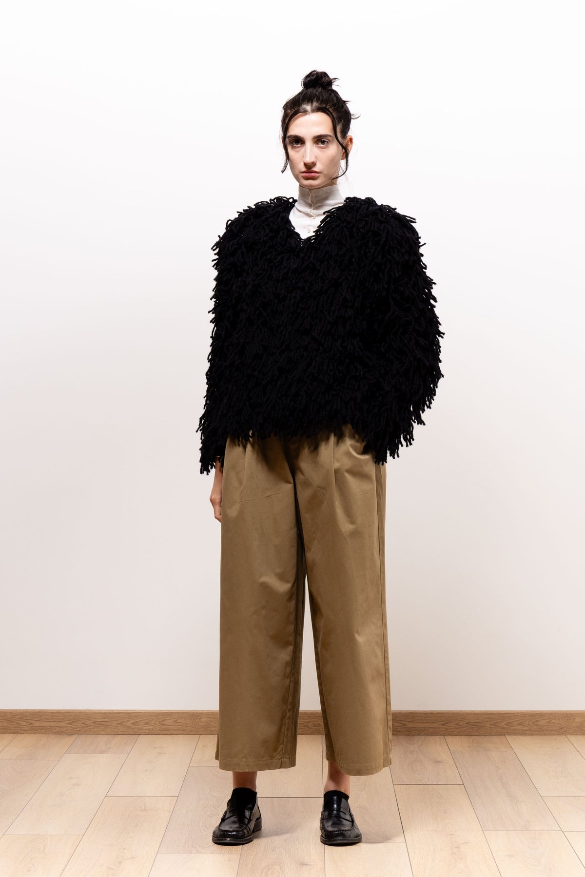 Front view of a model wearing khaki-brown Paulette Lee Trousers with a voluminous black textured top and black shoes, showing the pleated front and wide legs ending above the ankles.