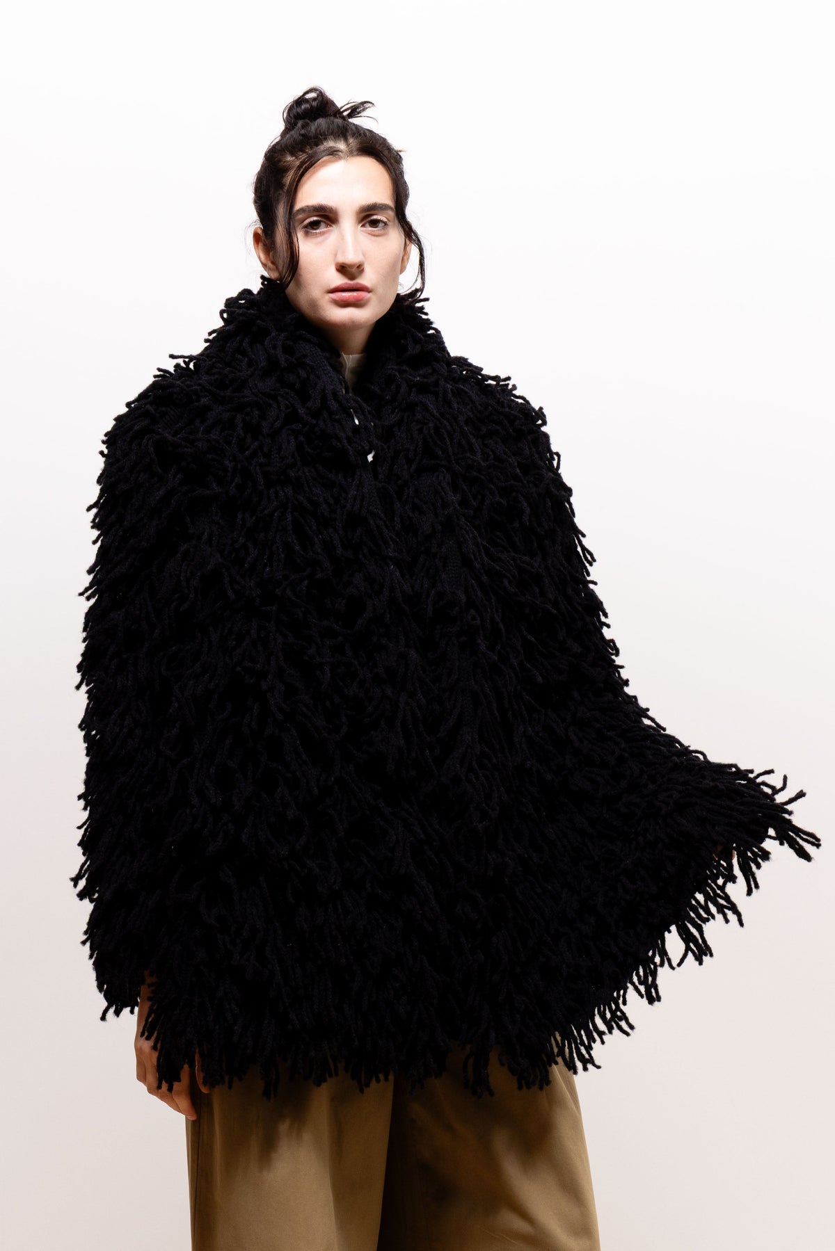 Model wrapped in the black Paulette Saint-Jean-de-Luz Oversize Scarf, showing its voluminous shaggy texture around the neck and torso, with one end extending outward at her side.
