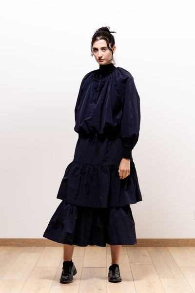 Three-quarter view of a model wearing the dark navy Paulette Georgia Top over a black high-neck layer with a matching tiered skirt, showing the full sleeves and loose fabric gathered at the hem.