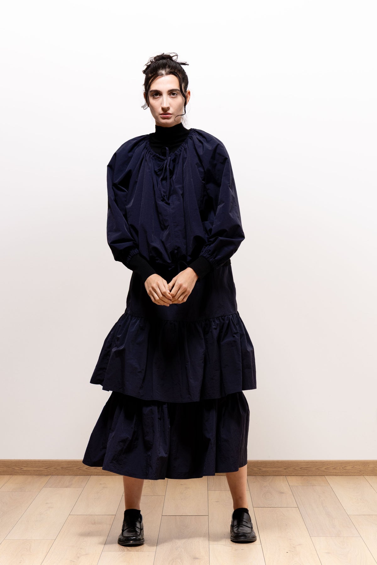 Front view of a model wearing the dark navy Paulette Georgia Top with a matching tiered skirt and black shoes, hands clasped at the waist, showing the neckline ties and rounded sleeves.