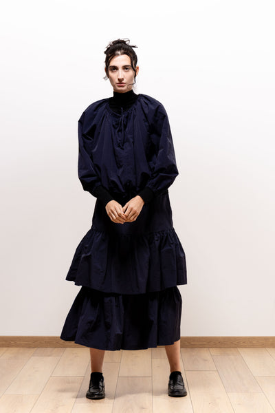 Front view of a model wearing the dark navy Paulette Georgia Top with a matching tiered skirt and black shoes, hands clasped at the waist, showing the neckline ties and rounded sleeves.