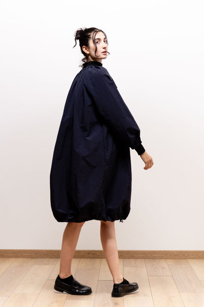 Model looking over her shoulder in the dark navy Paulette Georgia Dress, showing its loose rounded silhouette, full long sleeves with fitted cuffs, and gathered bubble hem near the knees, paired with black shoes.