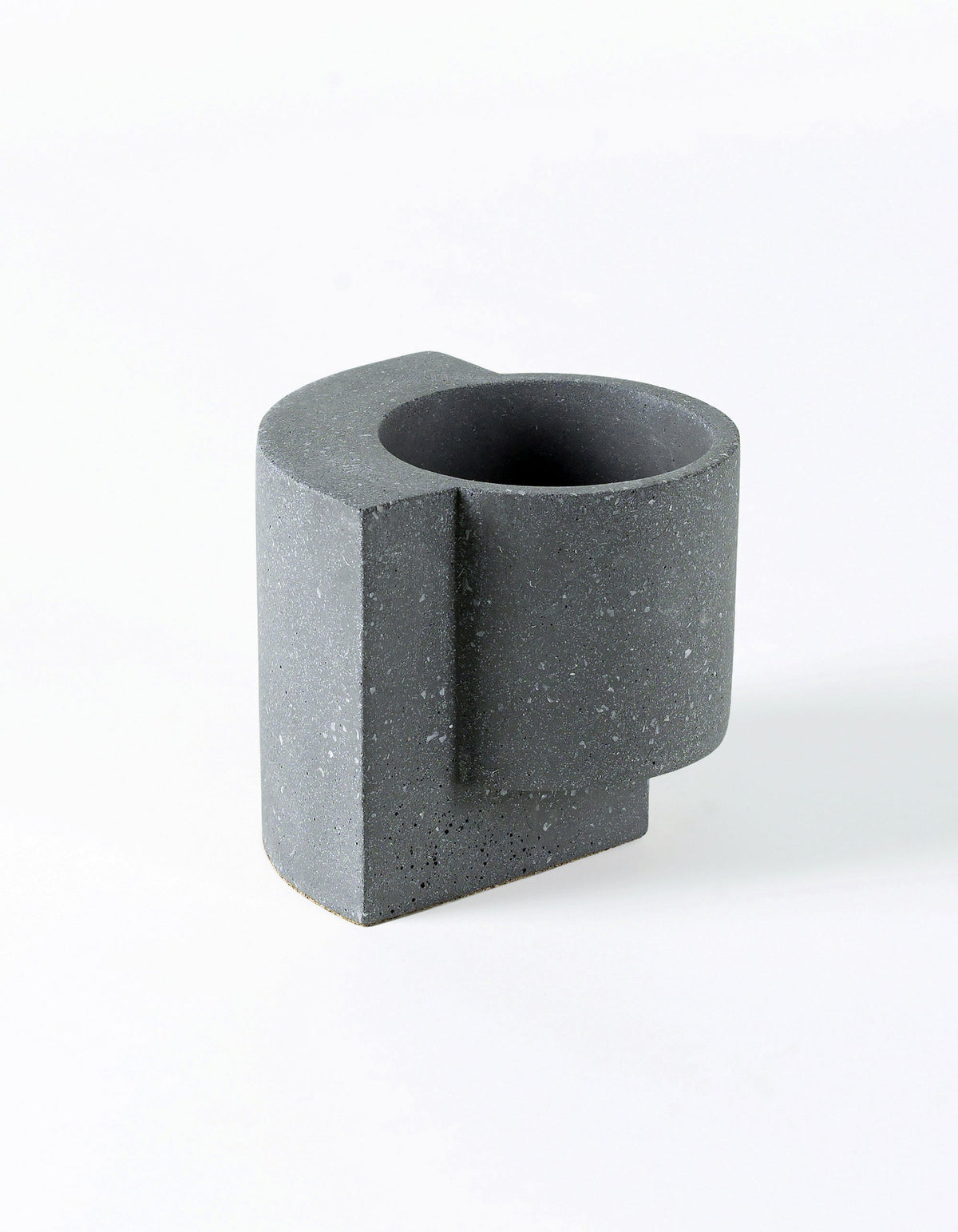 Graphite Tortuga Forma Platform Planter Small - Terrazzo viewed from above at an angle on white, showing its dark circular interior, cylindrical body, projecting vertical slab and scattered pale flecks.