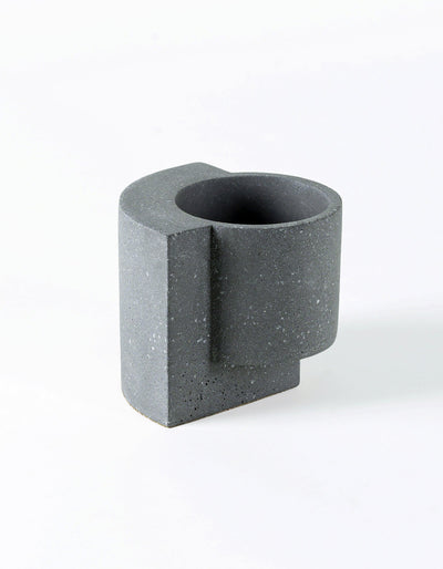 Graphite Tortuga Forma Platform Planter Small - Terrazzo viewed from above at an angle on white, showing its dark circular interior, cylindrical body, projecting vertical slab and scattered pale flecks.