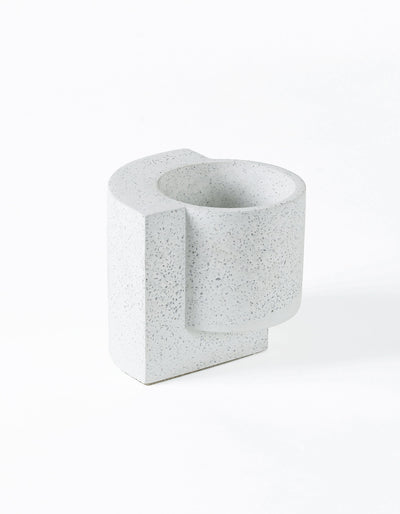 White Tortuga Forma Platform Planter Small - Terrazzo viewed at an angle on white, showing grey speckles, a deep round planting cavity and a flat slab extending along one side and beneath the cylindrical pot.