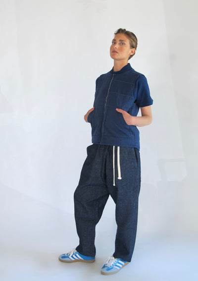 Model wearing a navy quilted zip-front vest over a matching blue shirt with loose dark drawstring pants and blue sneakers.